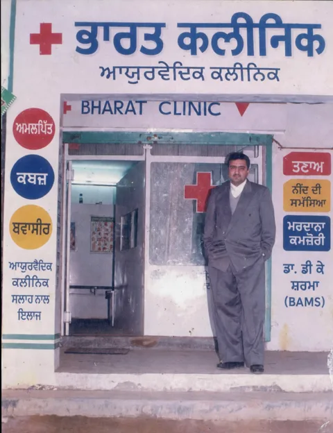 Dr. D. K. Sharma outside the Jugiana Phatak branch of Bharat Clinic in 1996, with the Punjabi signboard listing acidity, constipation, piles, nerves, sleep and men’s health